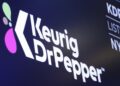 FILE - The logo for Keurig Dr. Pepper appears above a trading post on the floor of the New York Stock Exchange, July 12, 2018. (AP Photo/Richard Drew, File)